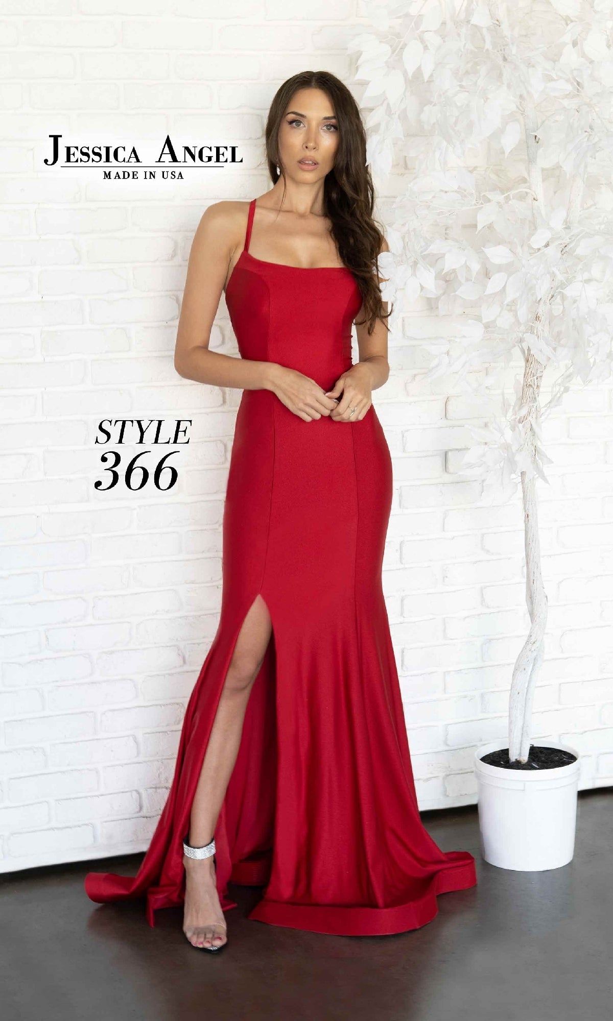 Woman wearing the Jessica Angel 366 Lace-Up Long Prom Dress—red, sleeveless, with an open back and high slit—stands indoors beside a white artificial tree.